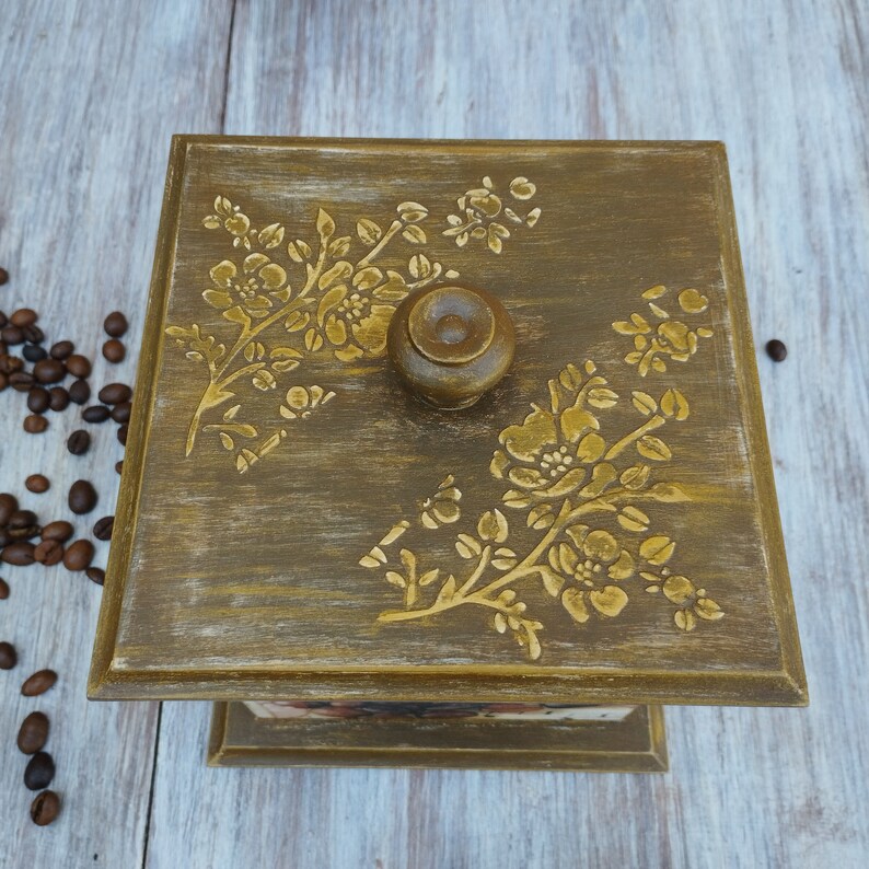 May include: A wooden box with a floral design painted on the top. The box has a wooden knob and is painted in a dark green color.