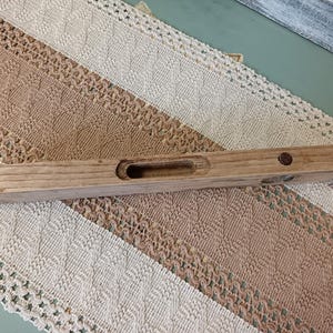 Pu&ograve; includere: Un livello in legno con un piccolo foro al centro. Il livello &egrave; in legno marrone chiaro e ha una macchia marrone scuro.