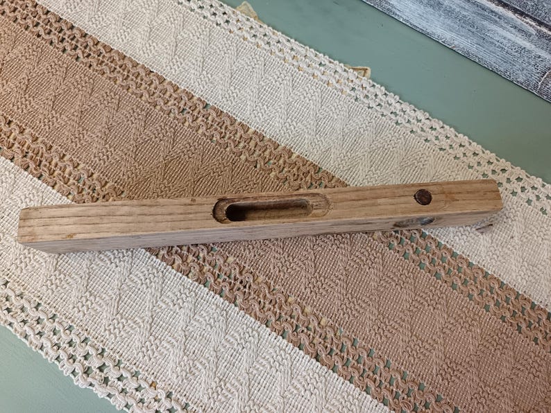 Pu&ograve; includere: Un livello in legno con un piccolo foro al centro. Il livello &egrave; in legno marrone chiaro e ha una macchia marrone scuro.