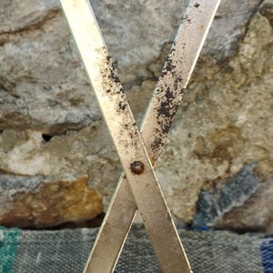 May include: Close-up of two crossed metal bars with a rusty patina. The bars are joined together with a metal rivet.