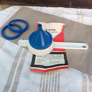 Op de afbeelding: Een witte plastic zeef met een blauwe trechter en een witte handgreep. De zeef is geëtiketteerd met "Sito Cezhivaniya" in het Russisch. De zeef wordt gebruikt voor het zeven van vloeistoffen.