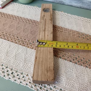 Pu&ograve; includere: Un blocco rettangolare di legno con un foro nella parte superiore, misurato con un metro a nastro per una lunghezza di circa 25 cm.