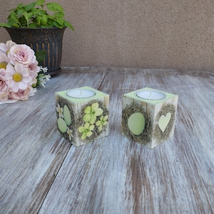 Może przedstawiać: Dwa białe drewniane świeczniki z wiosennym wzorem i jajkami. Świeczniki stoją na jasnym drewnianym blacie.