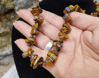 May include: A necklace made of tiger's eye stones with a brown and gold color. The stones are irregular in shape and are strung on a black cord.