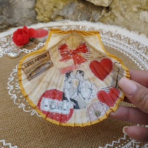 May include: A white seashell with a gold rim, decorated with red hearts, a red bow, a couple kissing, and a vintage ticket that says "Tunnel of Love." The shell is decorated with a gold key and the text "Love Potion."
