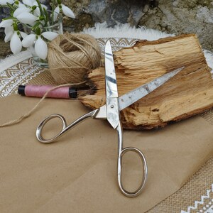 May include: Silver scissors with a wooden handle and a brown twine ball on a white and brown patterned surface.