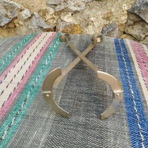 May include: A pair of silver metal tongs with rounded ends, crossed and lying on a striped fabric surface.