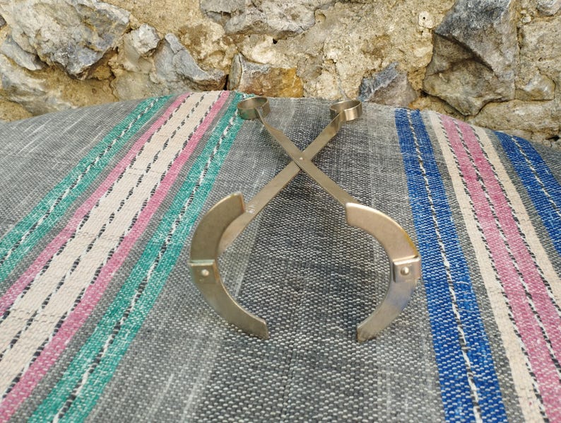May include: A pair of silver metal tongs with rounded ends, crossed and lying on a striped fabric surface.