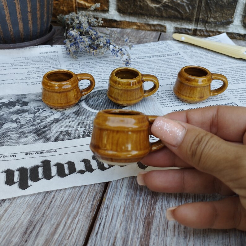Puede incluir: Cuatro peque&ntilde;as tazas de cer&aacute;mica marr&oacute;n con forma de barril y asas. Las tazas est&aacute;n sobre un fondo de peri&oacute;dico.