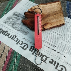Könnte beinhalten: Eine rote Metall-Küchenwaage mit einem Haken und einem Zifferblatt, das von 0 bis 10 geht. Die Waage ist mit "Can I make these Thai Chicken Skewers?" und "Skewers with coconut" beschriftet.