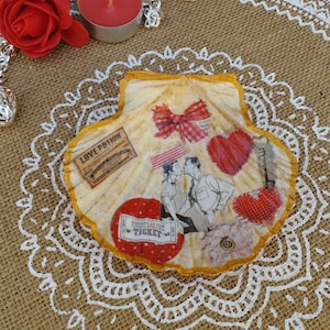 May include: A seashell decorated with a collage of vintage images, including a couple kissing, a red bow, a heart, and a ticket that says "Tunnel of Love Ticket".