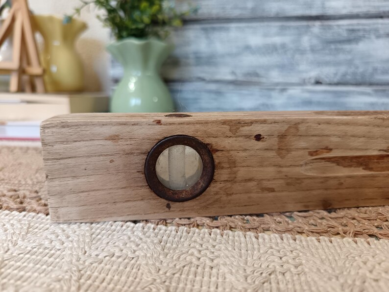 Pu&ograve; includere: Un livello a bolla in legno vintage con un visore a bolla in metallo arrugginito. Il livello &egrave; in legno marrone chiaro e ha una finitura naturale.