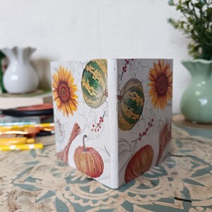 Puede incluir: Una caja de madera blanca con un dise&ntilde;o de oto&ntilde;o. La caja presenta calabazas, girasoles y calabacines en tonos naranja, amarillo, verde y marr&oacute;n.