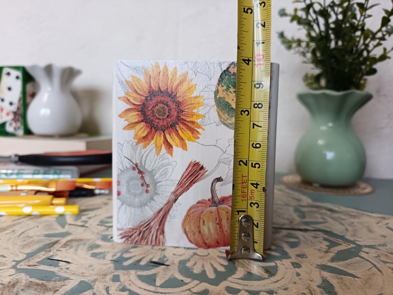 Puede incluir: Una caja de madera blanca con un dise&ntilde;o de oto&ntilde;o. La caja presenta un girasol, una calabaza y una calabaza. La caja mide 9 cm de alto.