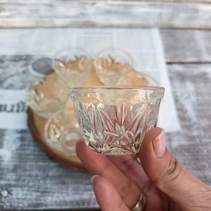 Può includere: Set di sei bicchieri di vetro trasparente con un motivo a diamante. I bicchieri sono disposti su un vassoio di legno.