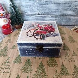 May include: A blue wooden box with a hinged lid and a metal clasp. The box is decorated with a vintage Christmas scene featuring Santa Claus riding in a sleigh pulled by reindeer. The scene is set against a snowy background.