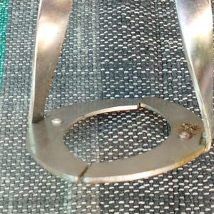 May include: A silver metal ring with a circular opening, designed to hold a coffee filter in place. The ring is made of two pieces that are joined together.