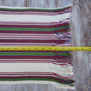 Pode incluir: Um tecido tecido com listras horizontais em creme, bord&ocirc;, verde e rosa. O tecido tem uma borda com franjas e mede aproximadamente 117 cm de comprimento.