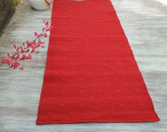 May include: Red table runner with a textured diamond pattern. The runner is made of a woven fabric and has a subtle sheen.