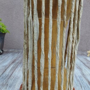 May include: Close-up of a wooden drum with vertical, light-coloured leather straps wrapped around the body. The drum has a natural wood finish, and the straps are textured. The drum is likely used for music and cultural events.