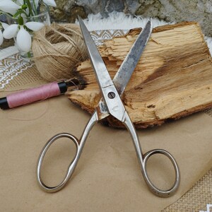 May include: A pair of vintage silver scissors with a wooden handle. The scissors have a small metal tag with the text "Germany" on it.