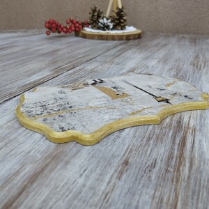 May include: A decorative wooden coaster with a gold trim and a white and gray design. The coaster has a unique, irregular shape.