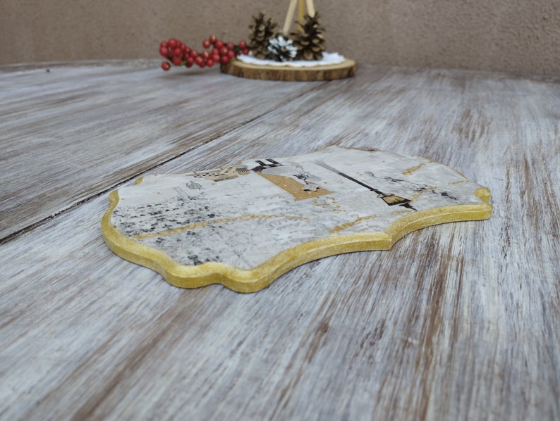 May include: A decorative wooden coaster with a gold trim and a white and gray design. The coaster has a unique, irregular shape.
