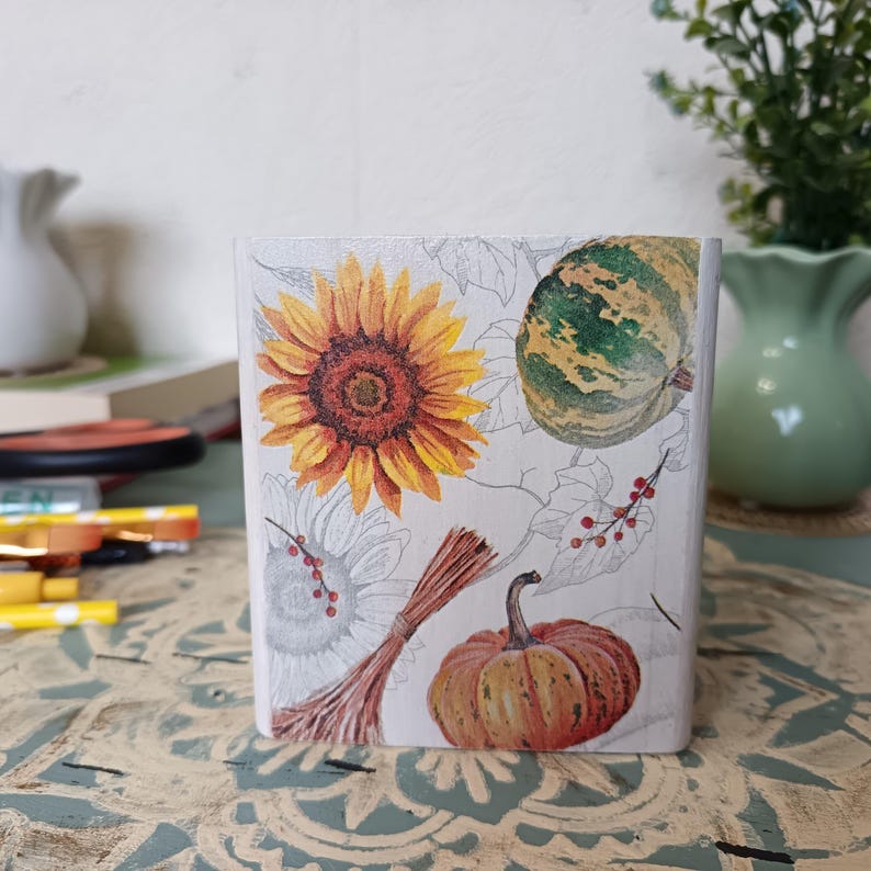 Puede incluir: Una caja de madera blanca con un dise&ntilde;o de tem&aacute;tica oto&ntilde;al. La caja presenta un girasol, una calabaza y una calabaza. El dise&ntilde;o est&aacute; impreso en la caja y tiene un aspecto vintage.