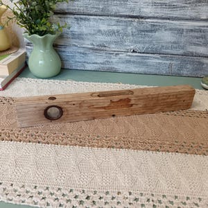 Pu&ograve; includere: Un livello in legno vintage con un livello a bolla circolare. Il livello &egrave; in legno invecchiato e ha una finitura naturale.