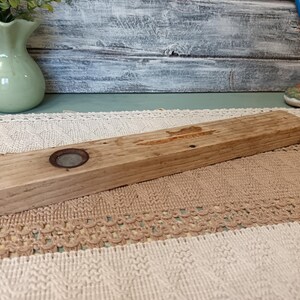 Pu&ograve; includere: Un ripiano in legno rustico con un anello di metallo al centro. Il ripiano &egrave; in legno naturale di colore marrone chiaro e ha una texture ruvida.
