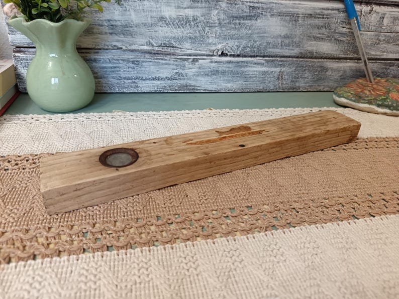 Pu&ograve; includere: Un ripiano in legno rustico con un anello di metallo al centro. Il ripiano &egrave; in legno naturale di colore marrone chiaro e ha una texture ruvida.