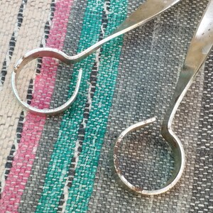 May include: Two silver metal rings with rounded edges. The rings are connected by a long, thin, silver metal rod.