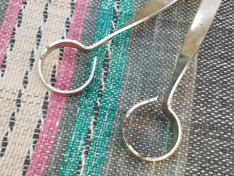 May include: Two silver metal rings with rounded edges. The rings are connected by a long, thin, silver metal rod.