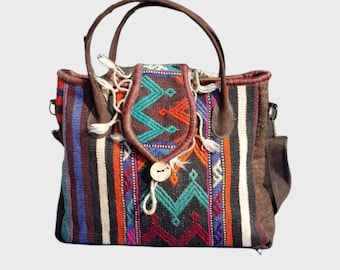 May include: A colorful woven tote bag with brown leather handles and accents. The bag features a geometric pattern in shades of blue, orange, and teal, with a wooden button closure and decorative tassels.