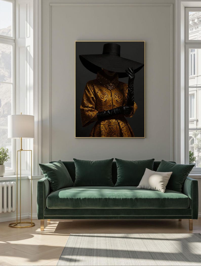 Op de afbeelding: Een ingelijste print van een vrouw die een grote zwarte hoed en een gouden, gepatroneerde jurk draagt. De vrouw staat voor een donkere achtergrond.