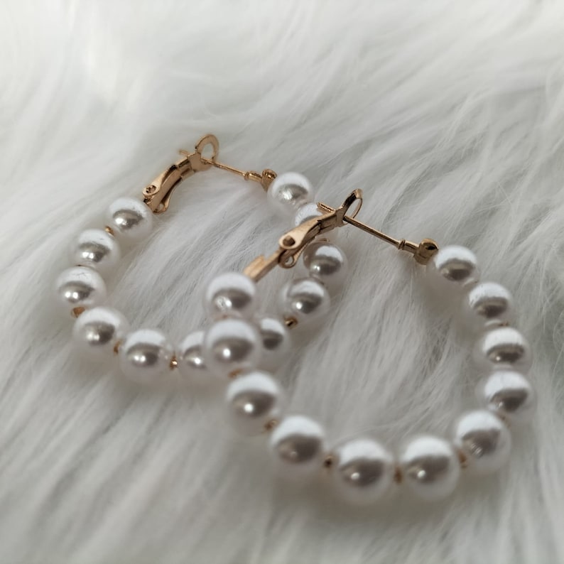 May include: A pair of gold hoop earrings with white faux pearl accents.
