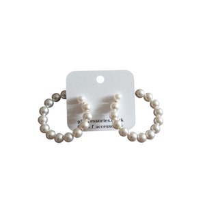 May include: A pair of white pearl hoop earrings. The earrings are made of small, round pearls that are strung together to form a hoop shape. The hoops are about 2 inches in diameter.
