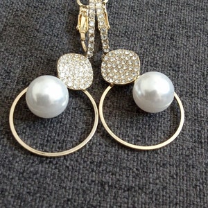 May include: A pair of gold hoop earrings with a pearl and a square-shaped crystal embellishment on each earring.