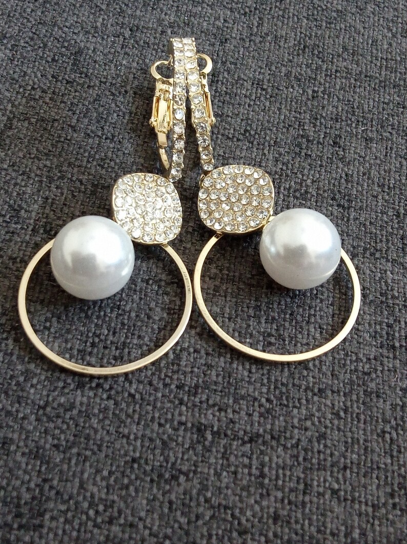 May include: A pair of gold hoop earrings with a pearl and a square-shaped crystal embellishment on each earring.