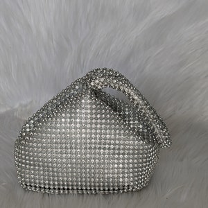 May include: A silver mesh clutch bag with a crystal-like design. The bag has a knotted handle.