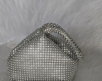 Könnte beinhalten: Eine silberne Mesh-Clutch mit einem kristallartigen Design. Die Tasche hat einen geknoteten Griff.