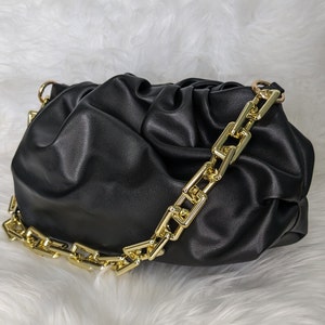 May include: Black leather handbag with a gold chain strap. The bag has a gathered, or 'cloud' design.
