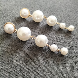 May include: A pair of long, dangling earrings with multiple white pearl beads connected by gold chains.