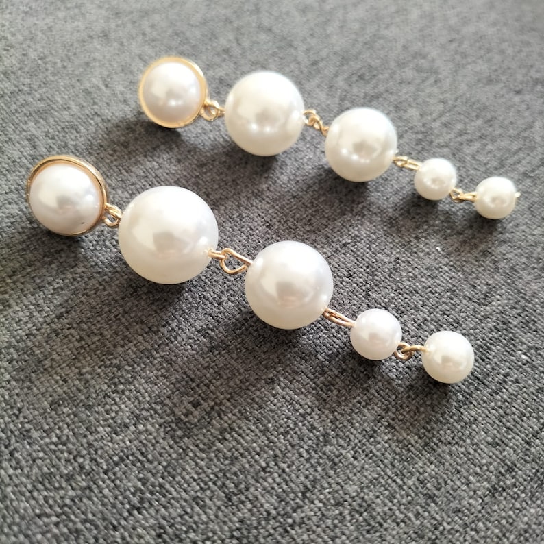 May include: A pair of long, dangling earrings with multiple white pearl beads connected by gold chains.