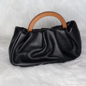 May include: A black leather handbag with a brown wooden top handle. The bag has a gathered, pleated design.