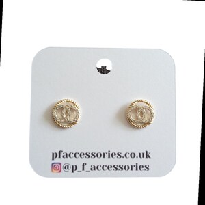 May include: Gold-tone earrings with a double-C design, set with clear cubic zirconia stones. The earrings are displayed on a white card with the text "pfaccessories.co.uk" and "@p_f_accessories".