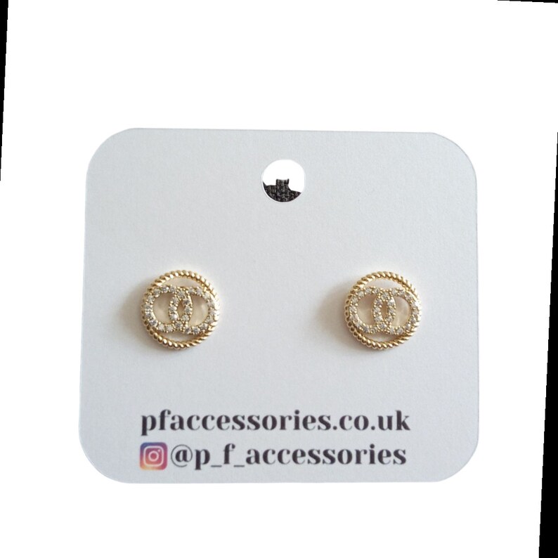 May include: Gold-tone earrings with a double-C design, set with clear cubic zirconia stones. The earrings are displayed on a white card with the text "pfaccessories.co.uk" and "@p_f_accessories".