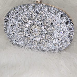 May include: A silver oval-shaped clutch purse covered in sparkling rhinestones.