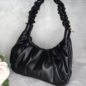 May include: A black, faux leather handbag with a gathered, pleated design. The bag has a single, adjustable, gathered strap.