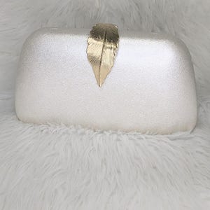 May include: A silver clutch purse with a gold leaf design on the front.